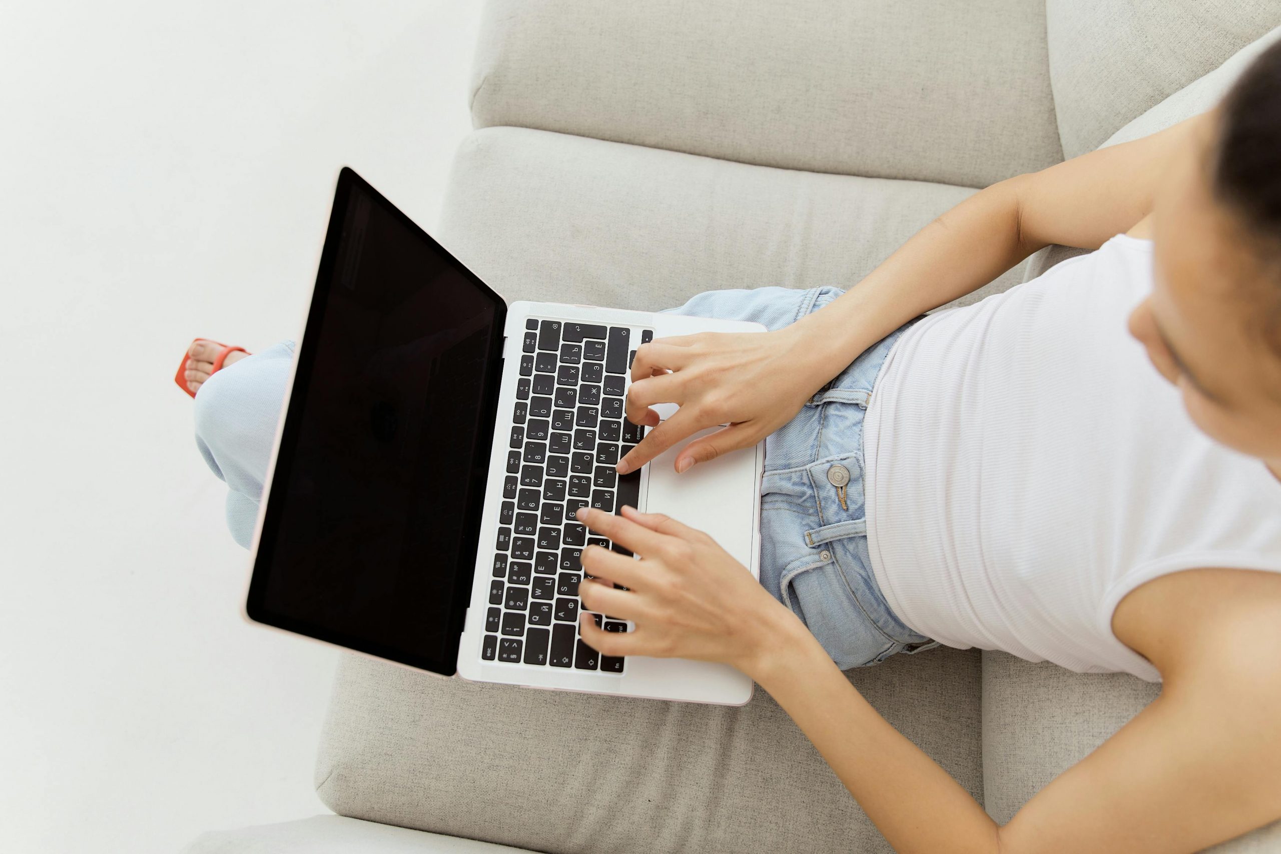 Overhead view of woman typing on laptop while sitting on a comfortable sofa indoors.