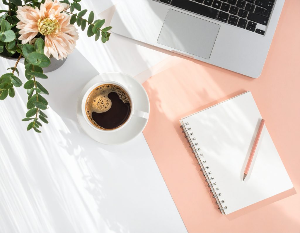 Schreibtisch mit Kaffeetasse, Blumen,  Notizblock und Laptop